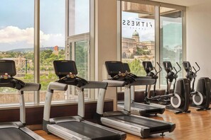 A gym with treadmills and elliptical machines, large windows with a view of a cityscape.