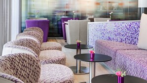 A modern lounge area with patterned sofas, round tables, and purple accents. - IntercityHotel Rostock (Rostock)