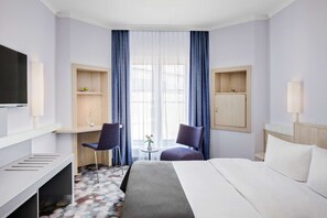A hotel room with a bed, a desk, two chairs, a TV, a small table with a vase, and a window with curtains.