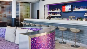 A modern bar area with a curved counter, bar stools, and a television screen displaying a menu. - IntercityHotel Rostock (Rostock)