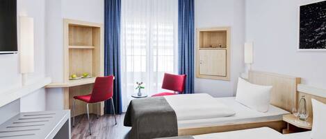 A hotel room with two beds, a desk, a chair, and a TV.
