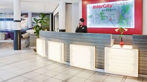 A hotel reception area with a large digital map display, a reception desk, and a seating area with bar stools. - IntercityHotel Rostock (Rostock)