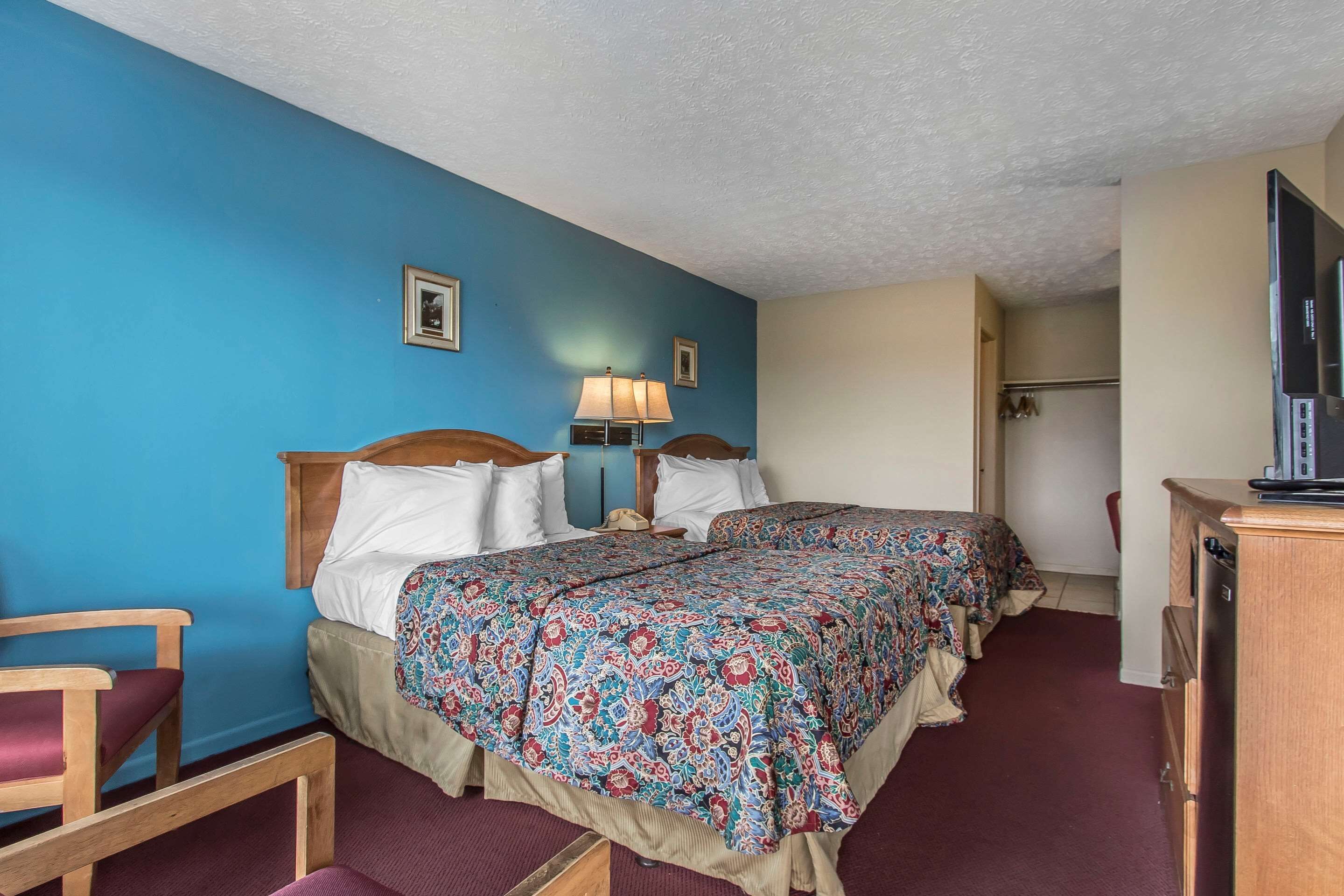 A hotel room with two beds, a wooden chair, a desk, and a television.