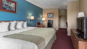 A hotel room with a large bed, a TV on a wooden dresser, a chair, and a desk with a lamp. - Rodeway Inn Jackson Northwest (Jackson)