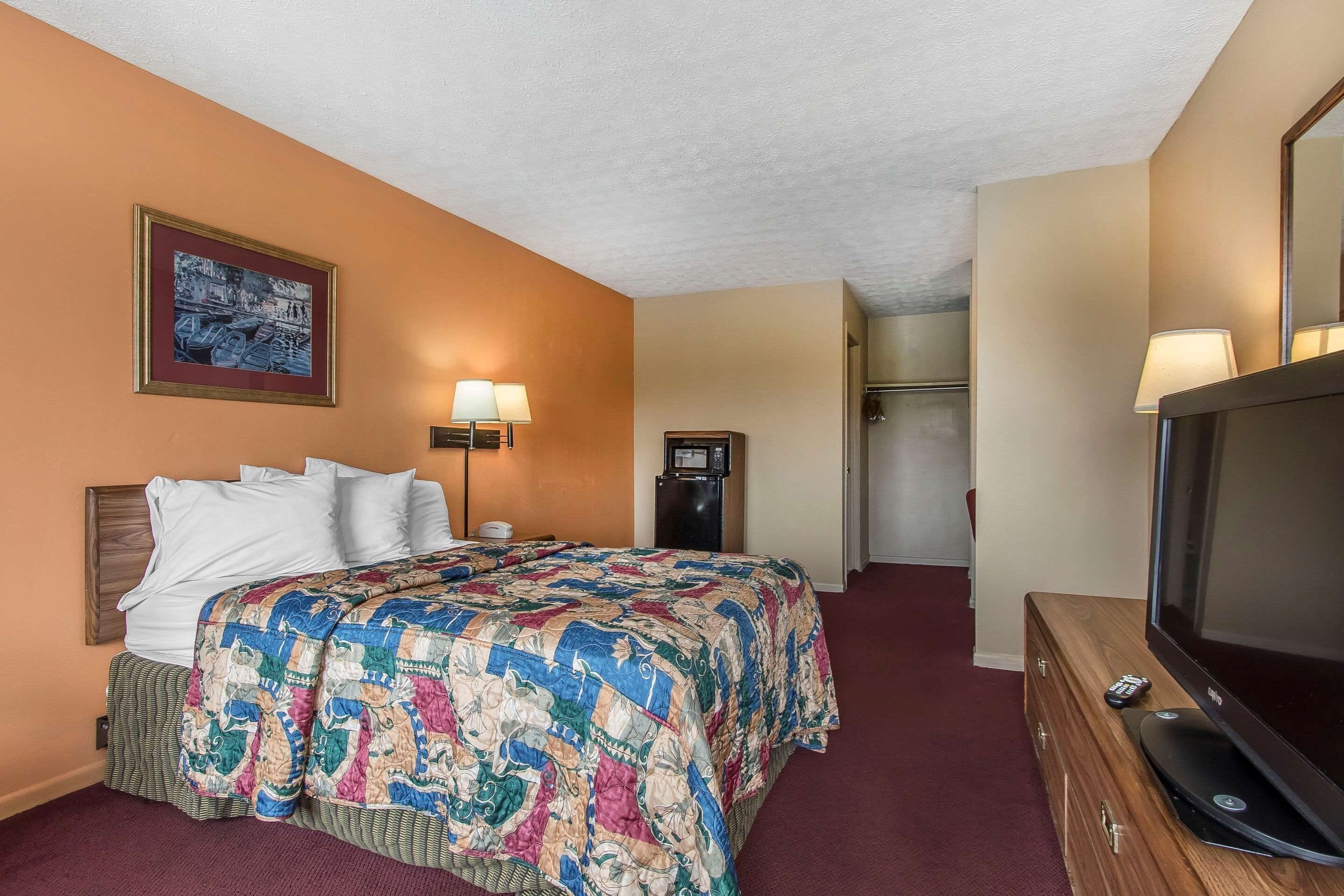 A hotel room with a bed, a television, a dresser, a lamp, and a painting on the wall.