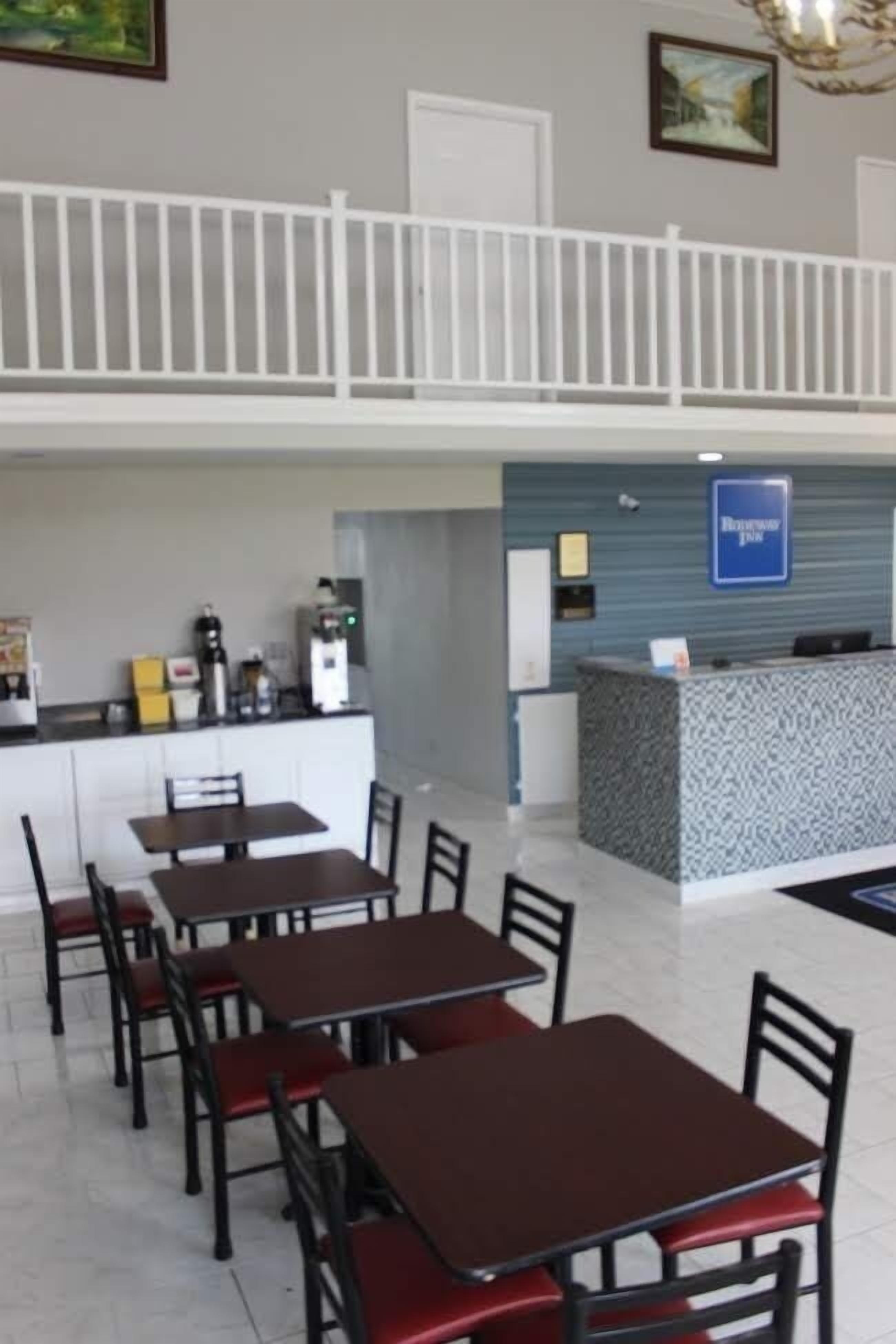 A hotel lobby with a reception desk, a counter with a coffee machine, and several tables and chairs.
