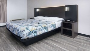 A modern hotel room with a large bed, a bedside table with a phone and remote, and a wall-mounted light fixture. - Motel 6 Fort Worth, TX - Downtown East (Fort Worth)