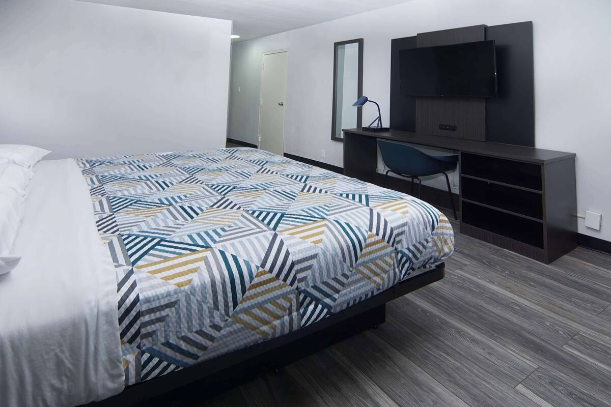 Una camera d'albergo moderna con un letto grande, una scrivania, una sedia e una TV a parete.