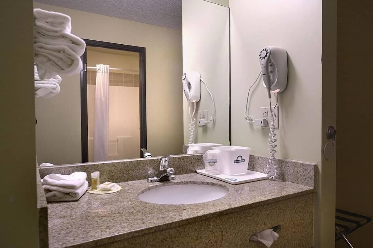 A hotel bathroom with a granite countertop, a sink, a mirror, a hairdryer, and a towel rack.
