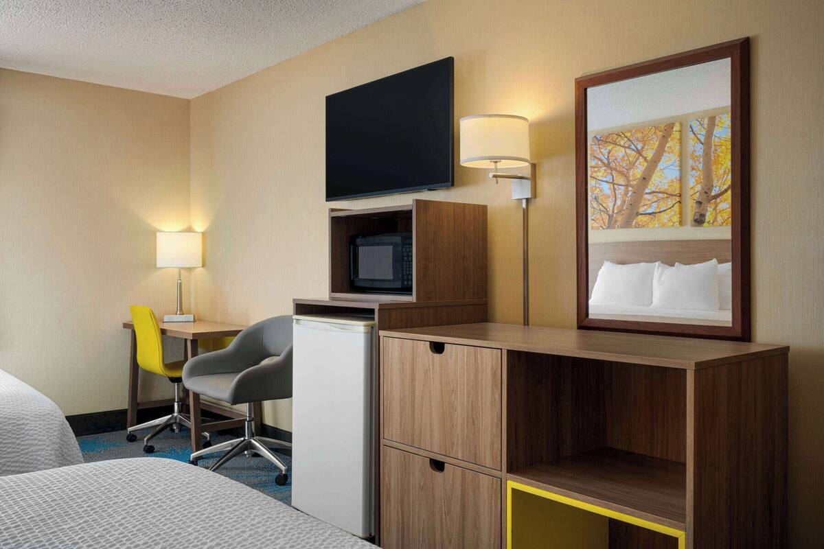 A hotel room with a bed, a desk with a computer, a chair, a TV, and a lamp.