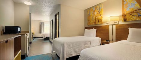 A hotel room with two beds, a desk with a television, a bathroom, and a hallway leading to another room.