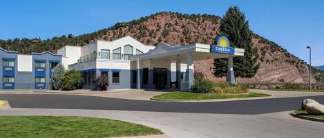A Days Inn with a modern design, a gas station, and a hilly backdrop.