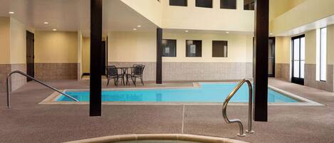 Une piscine intérieure à l’eau claire, entourée d’un sol et de murs carrelés, avec un espace détente et un escalier en arrière-plan.
