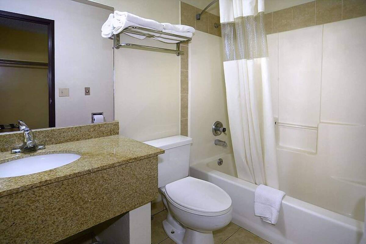 A bathroom with a granite countertop sink, a toilet, a bathtub, and a shower curtain.