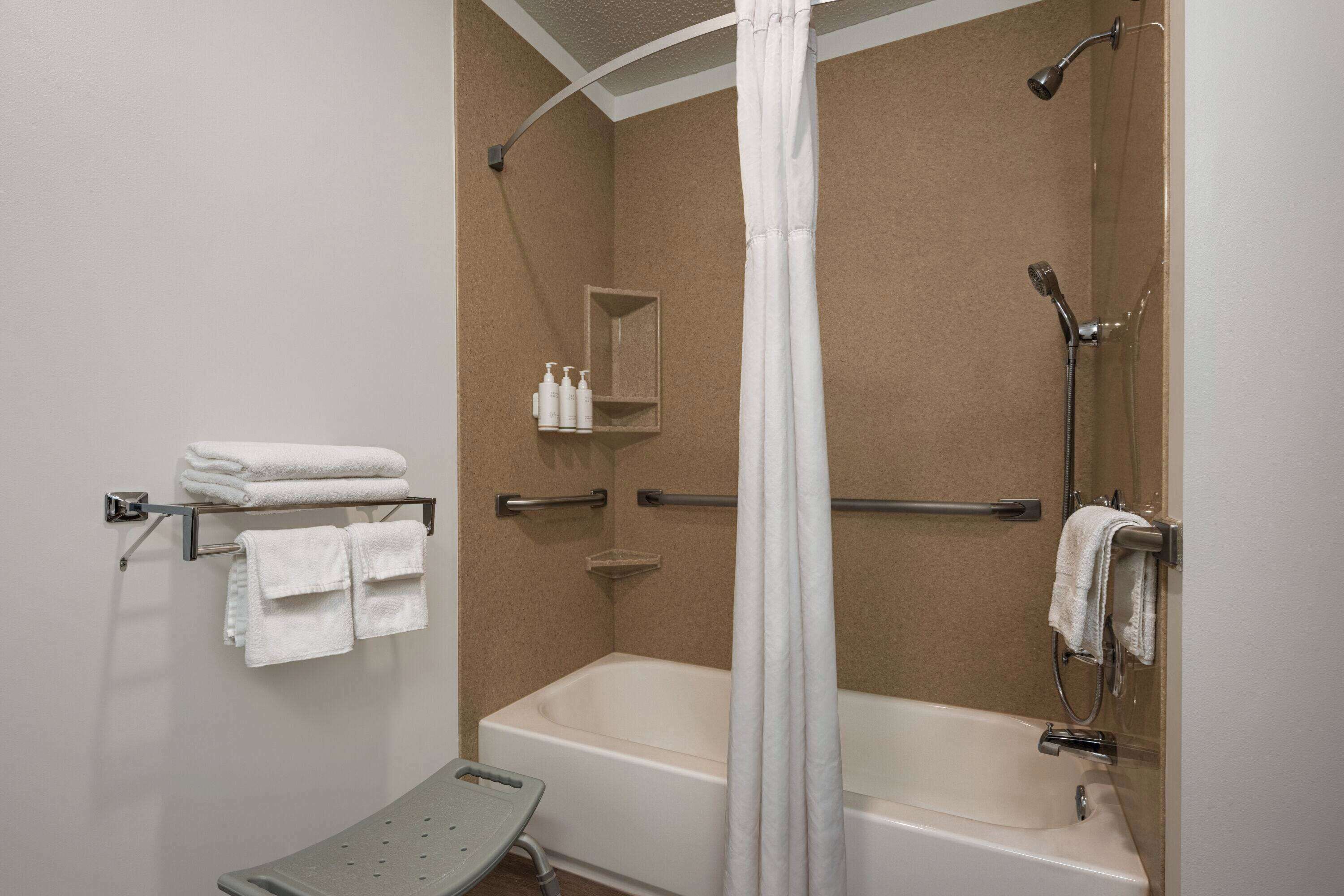 Une salle de bain avec une baignoire, une douche et un petit banc. Des serviettes et des articles de toilette sont disposés sur des étagères.