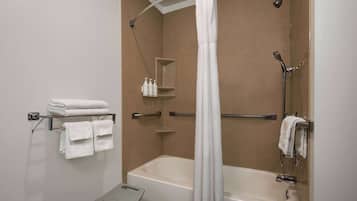 Une salle de bain avec une baignoire, une douche et un petit banc. Des serviettes et des articles de toilette sont disposés sur des étagères.