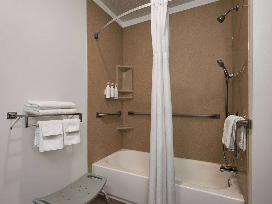 Une salle de bain avec une baignoire, une douche et un petit banc. Des serviettes et des articles de toilette sont disposés sur des étagères.