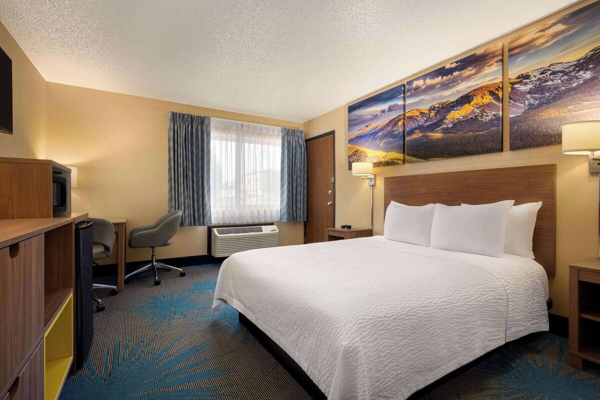 A hotel room with a large bed, a desk with a chair, a TV, and a painting on the wall.