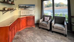 A kitchen with wooden cabinets, a marble countertop, a large window with a view of a road and greenery, and two upholstered chairs. - Inn By the Bay Monterey (Monterey)