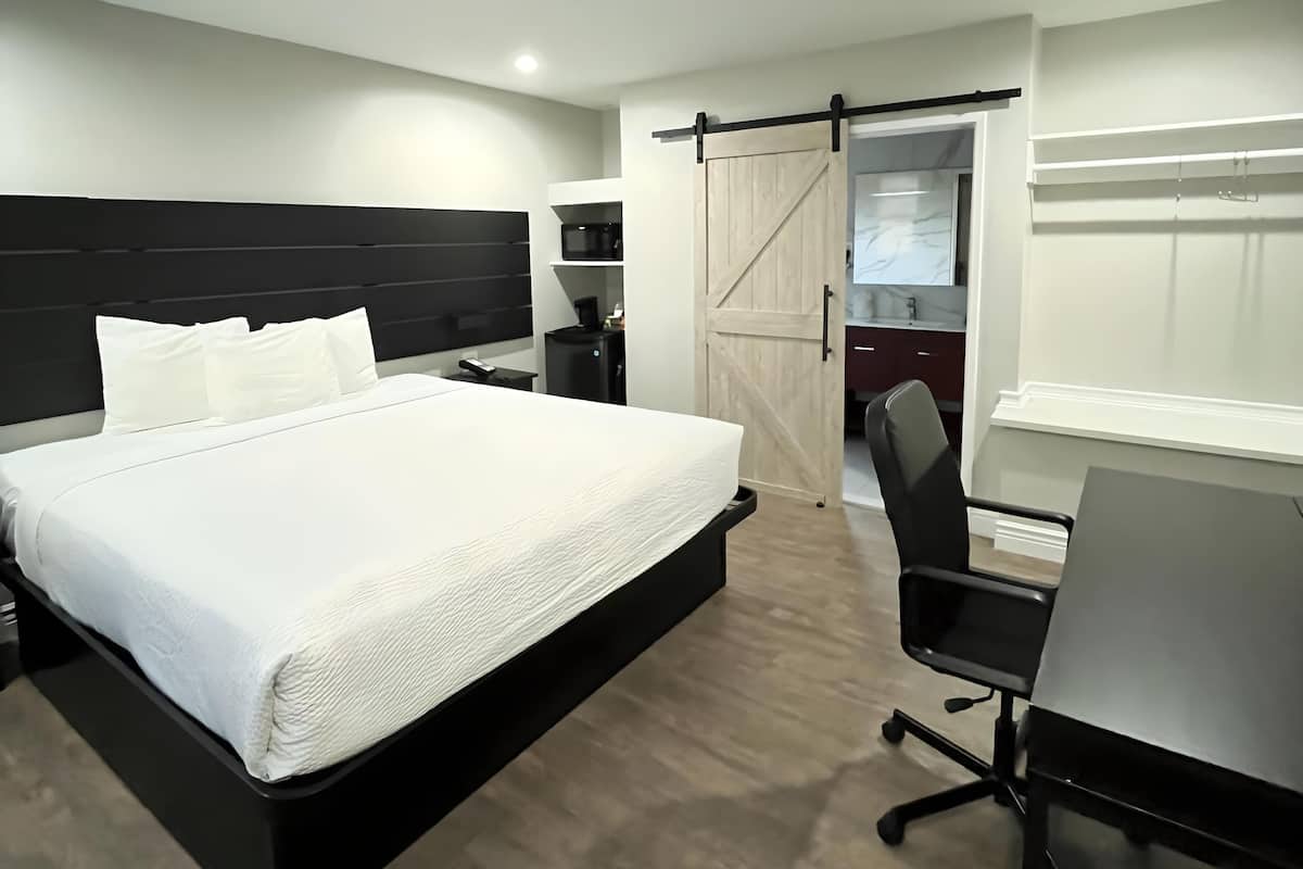 A modern hotel room with a large bed, a desk, and a sliding door closet.