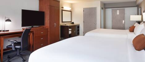 Una habitación de hotel con una cama grande, un escritorio con televisor, una silla, armario, espejo y puerta.