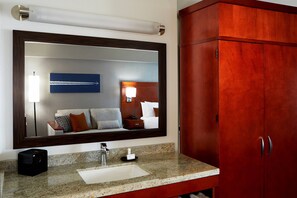 Un baño con un espejo grande, encimera de granito, lavamanos, dispensador de toallas y un mueble de madera.