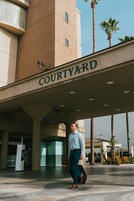 Un uomo che cammina verso un edificio con la scritta "COURTYARD", sullo sfondo cielo sereno e palme.