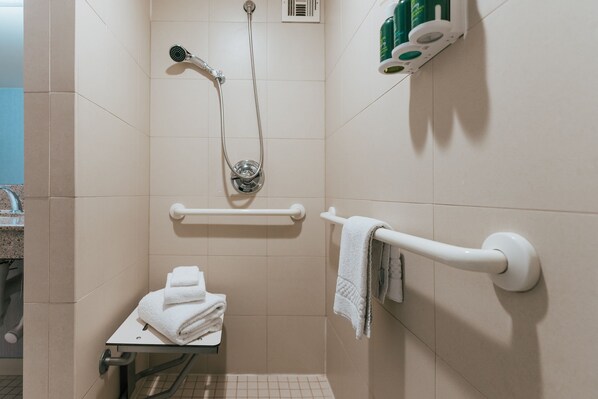 A bathroom with a shower, a towel rack, and a shelf with toiletries. - Courtyard by Marriott Los Angeles LAX/Century Boulevard (Los Angeles)