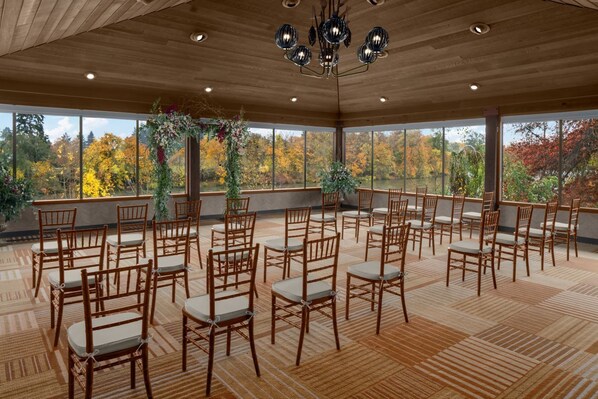 A spacious indoor area with wooden flooring and a large window overlooking a forested area.