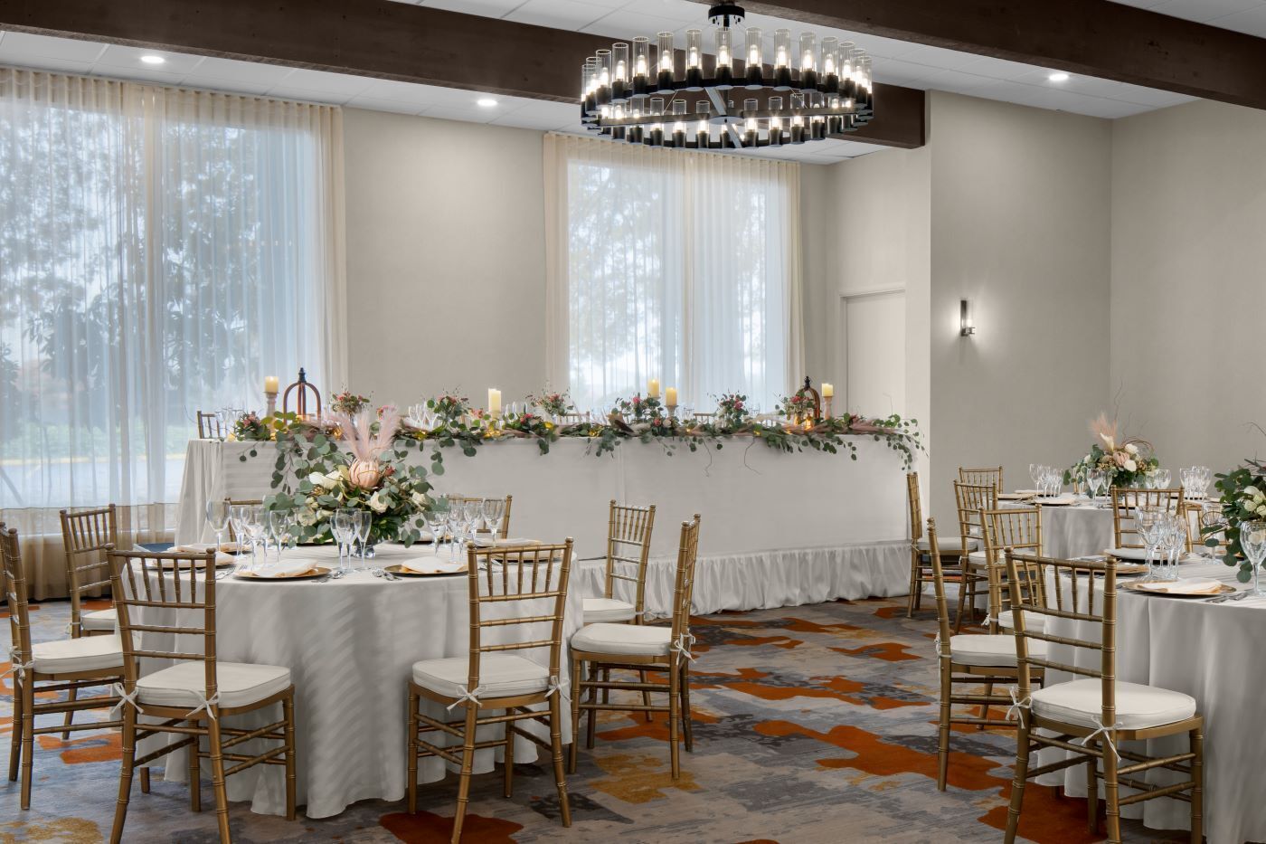 A banquet hall with round tables, white tablecloths, and bamboo chairs.