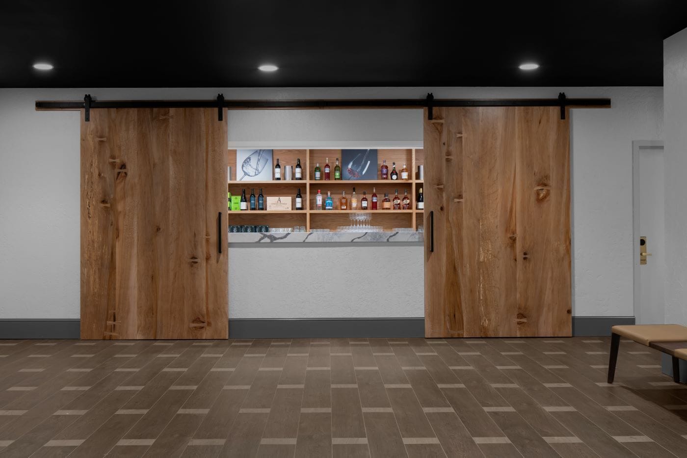 Una habitación con puerta corredera de madera, una zona de bar con estantes llenos de botellas y un banco.
