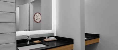 Een moderne badkamer met een zwart aanrecht, een houten wastafelmeubel, een spiegel en een klok aan de muur.
