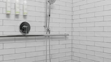 Un espace douche avec des murs et un sol recouverts de carreaux blancs, une douchette à main, un robinet mural et un distributeur de savon.