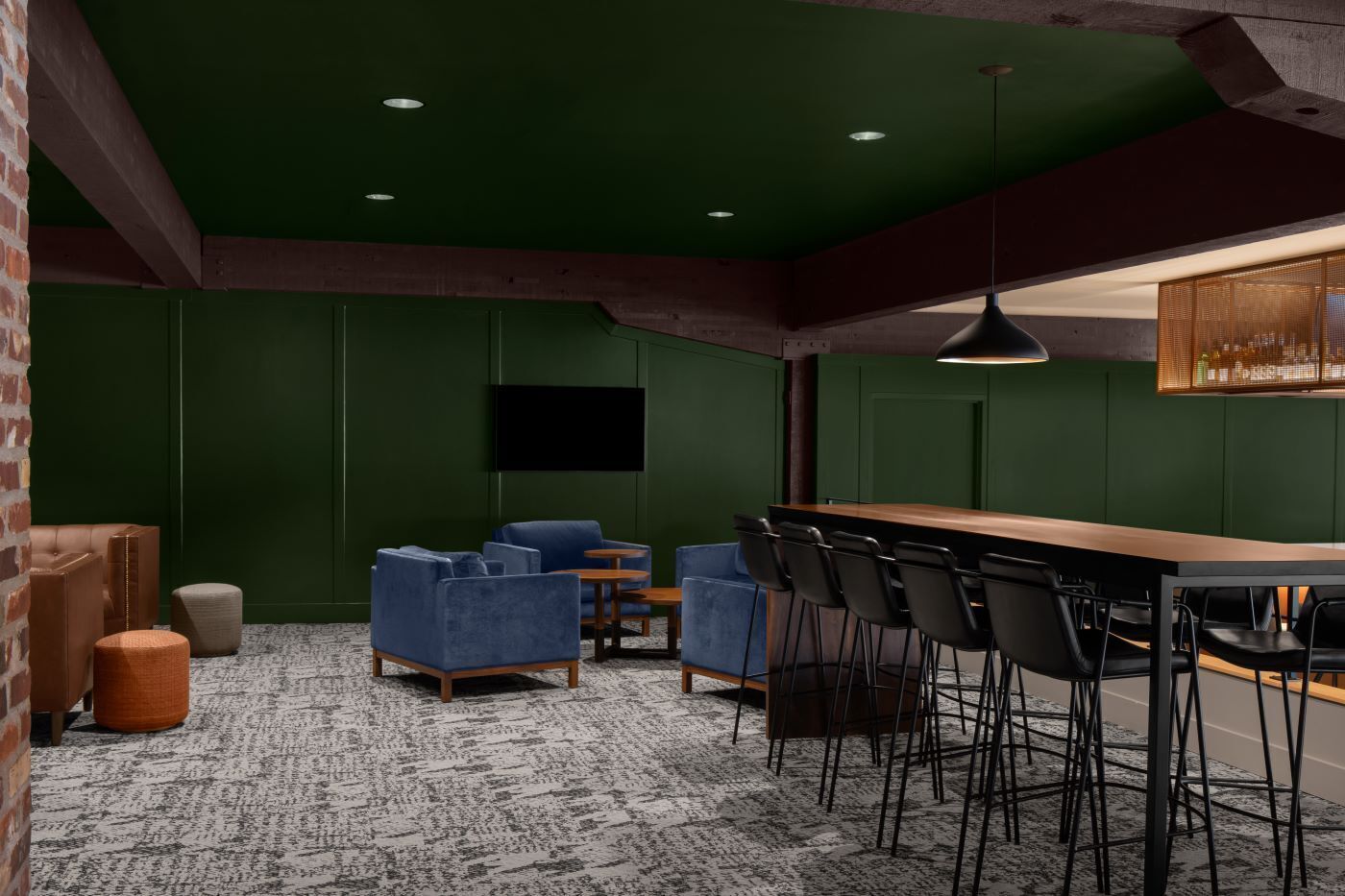 A modern bar area with green walls, a wooden bar counter, and black bar stools.