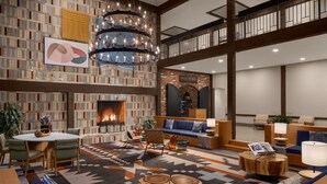 A spacious lobby with a fireplace, a seating area with sofas and chairs, a large chandelier, and a high ceiling with exposed beams.