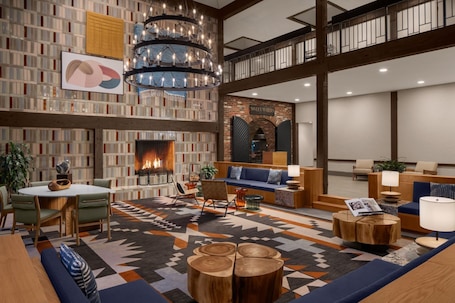 A spacious lobby with a fireplace, a seating area with sofas and chairs, a large chandelier, and a high ceiling with exposed beams.