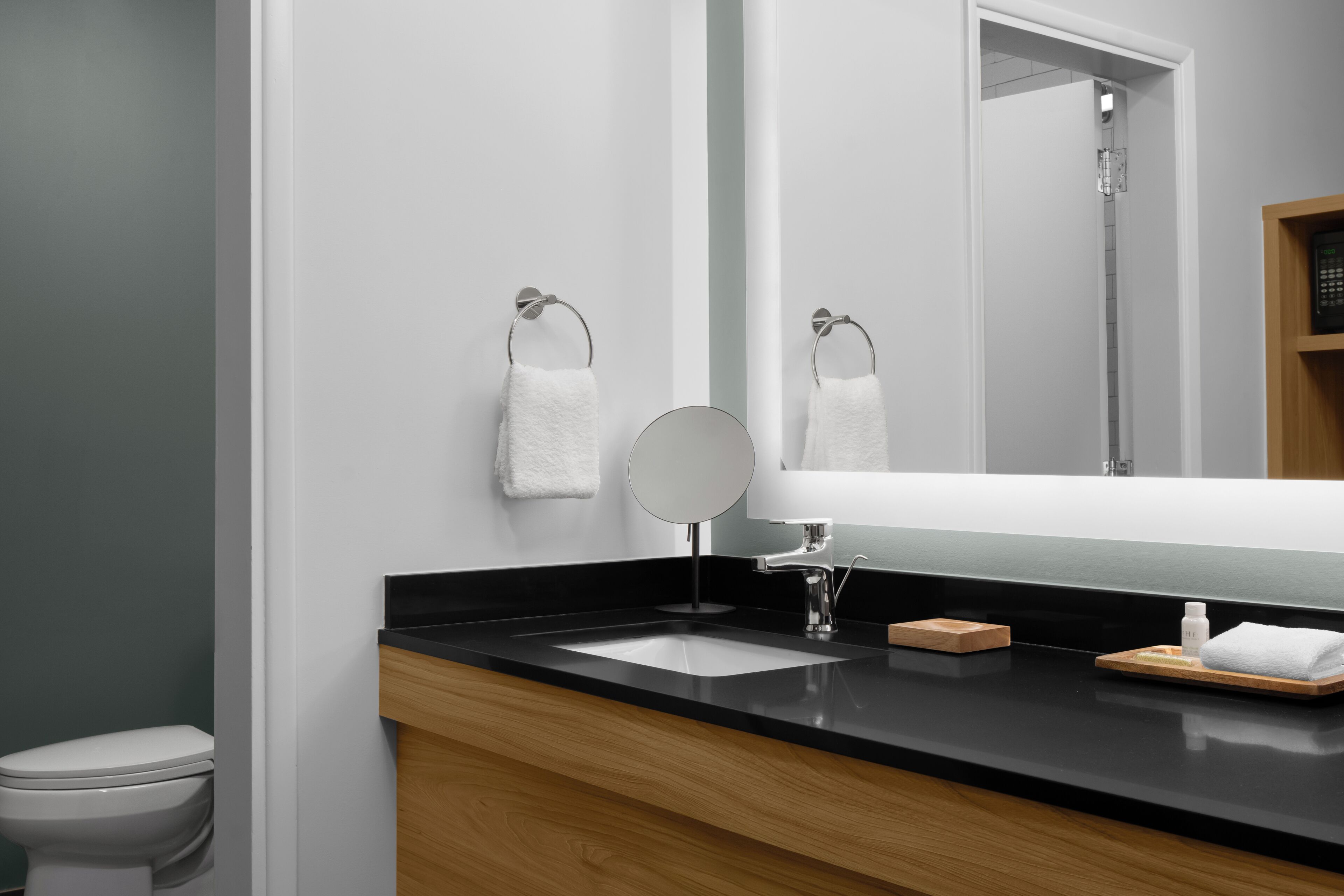 A modern bathroom with a black countertop, a round mirror, and two white towels hanging on towel rings.