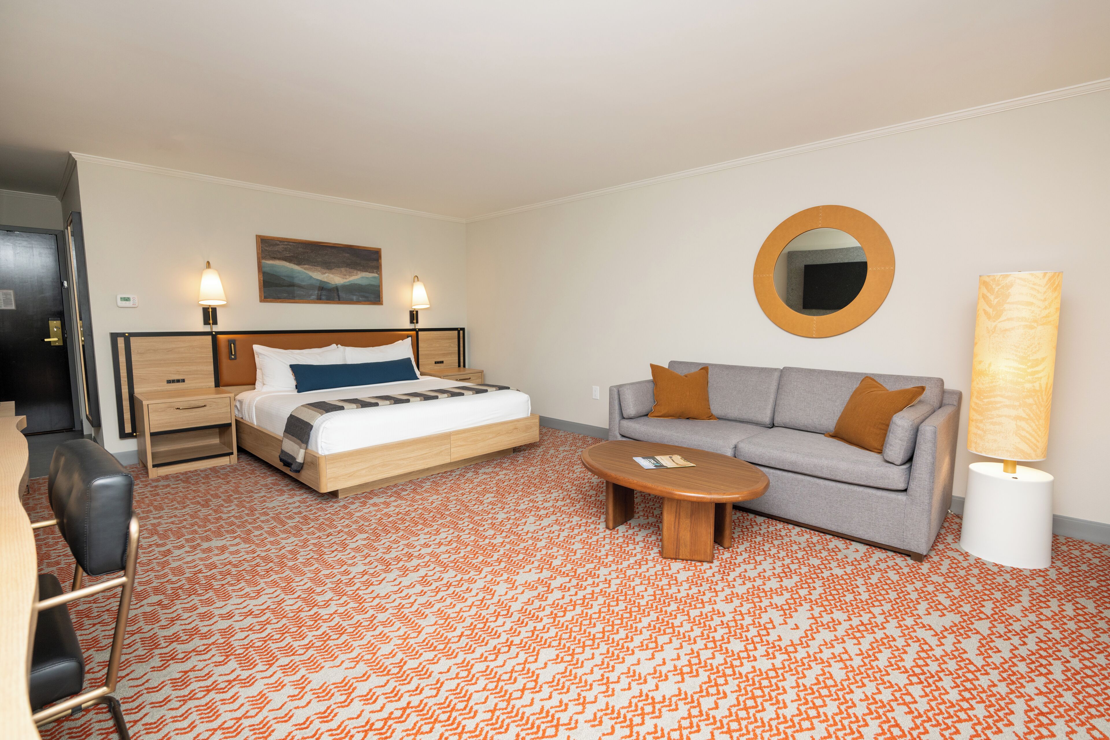 A hotel room with a bed, a sofa, a coffee table, a desk, and a lamp.