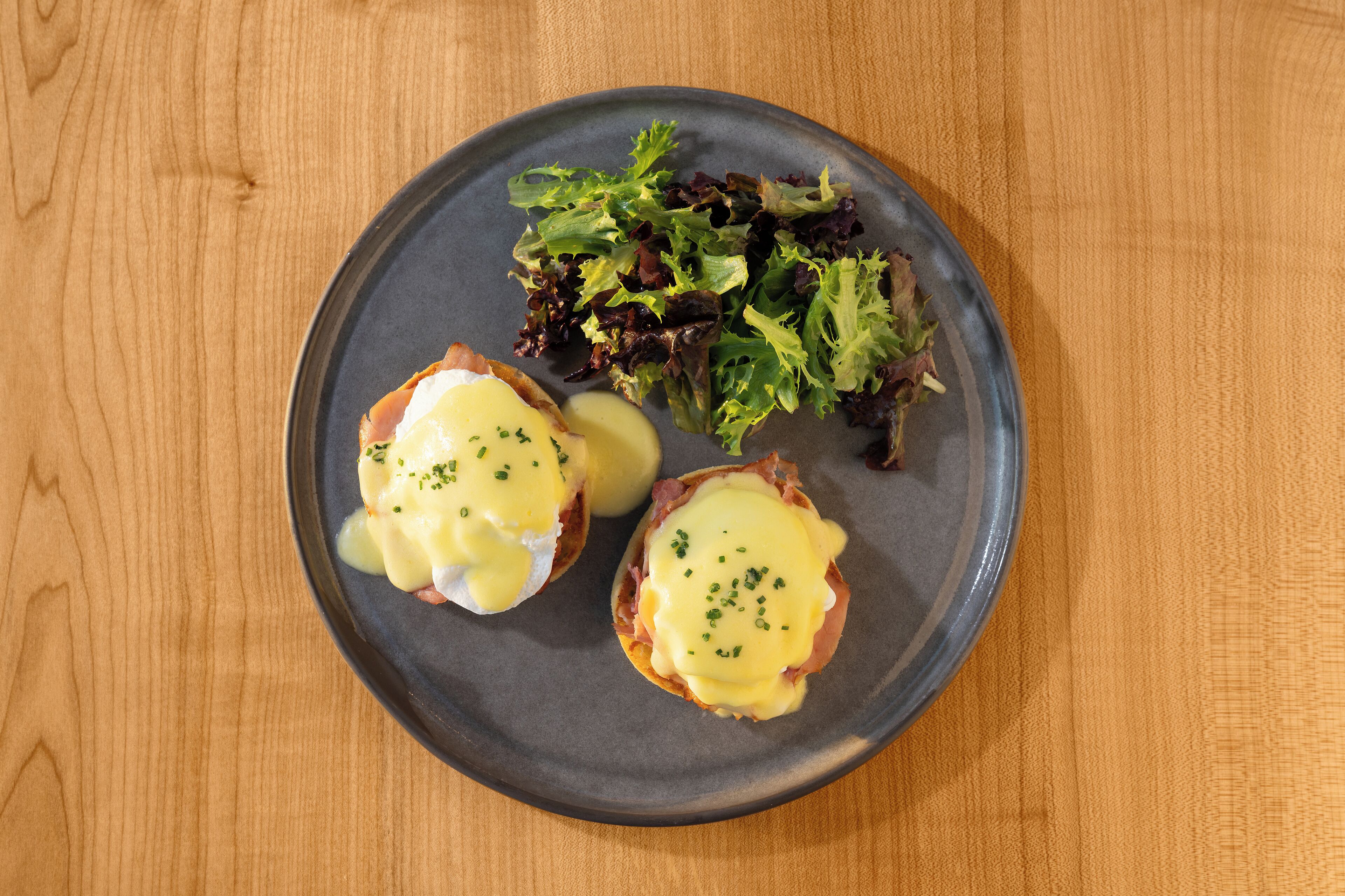 A plate with eggs benedict and a side salad on a wooden table.