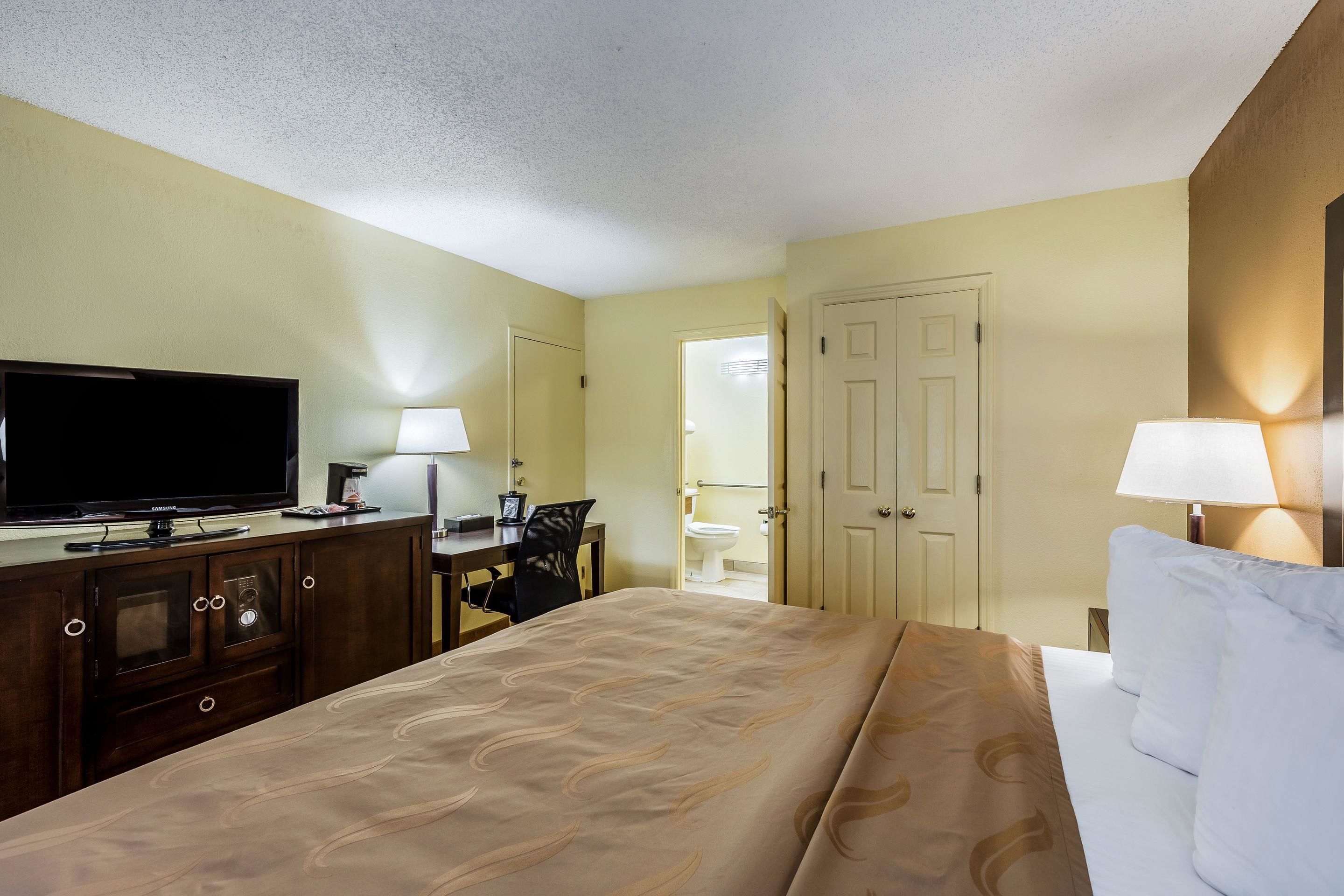 Habitación de hotel con cama, televisor, escritorio con silla y baño visible a través de una puerta abierta.