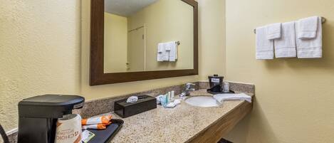 Un baño de hotel con encimera de granito, cafetera, lavamanos y espejo.