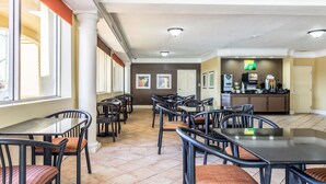 A spacious indoor area with multiple tables and chairs, a reception desk, and a kitchen in the background.