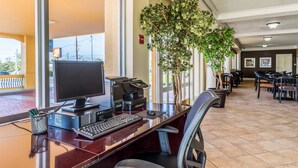 A hotel reception desk with a computer, printer, and telephone. There are chairs and tables in the background.