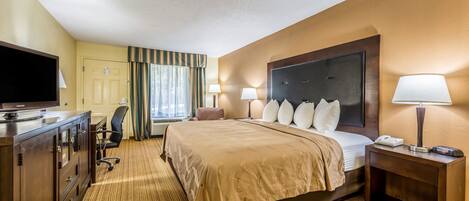 Una habitación de hotel con una cama grande, un escritorio con televisor de pantalla plana, una silla, una mesita de noche con lámpara y una ventana con cortinas.