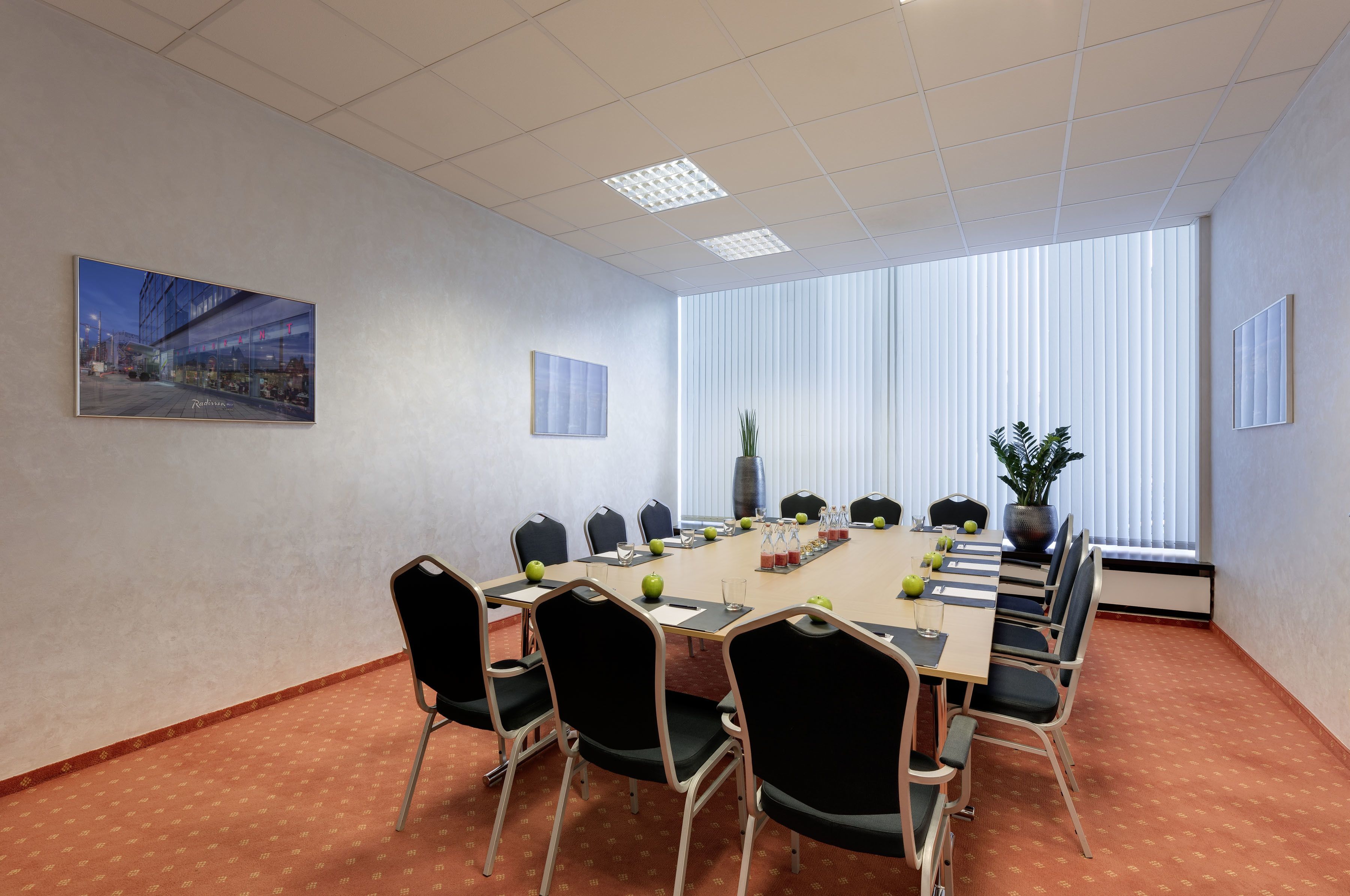 A conference room with a large table, chairs, a plant, and a painting on the wall.