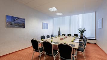 A conference room with a large table, chairs, a plant, and a painting on the wall.