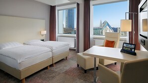 A hotel room with two beds, a small table, a chair, a TV, and a window with a city view.