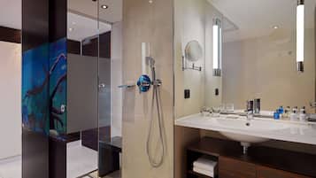 Un baño moderno con mampara de cristal, un espejo grande y un tocador con lavabo y artículos de aseo.