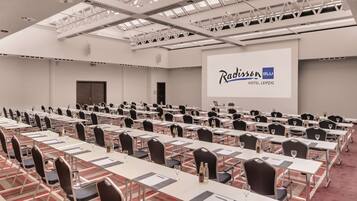 A conference room at Radisson Blu Hotel, Leipzig with multiple tables, chairs, and a large screen displaying the hotel name.