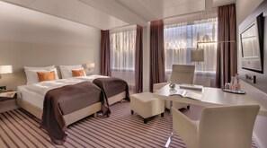 A hotel room with two beds, a desk, a chair, a TV, and a window with curtains.